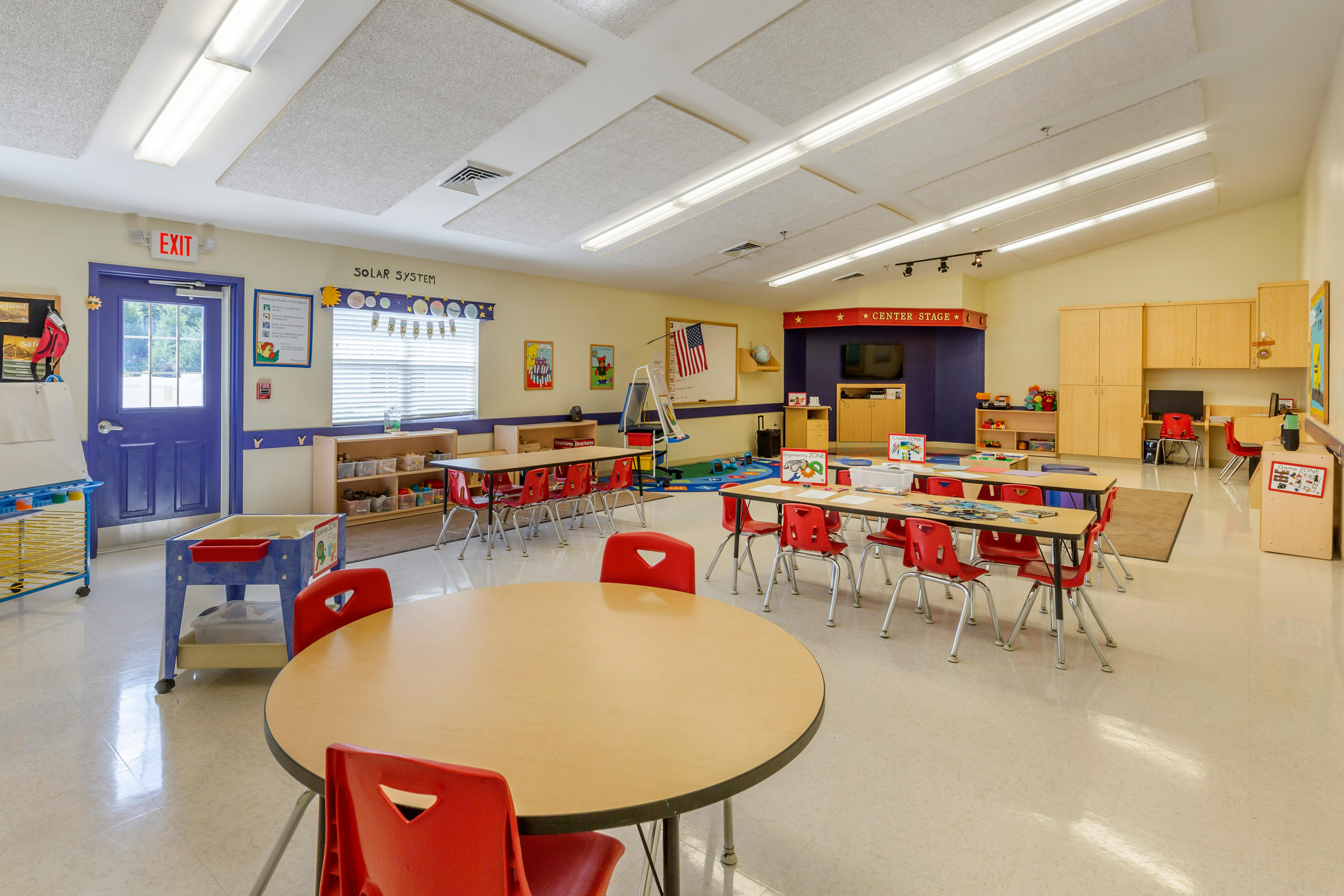An empty classroom with small tables and chairs, and various learning stations