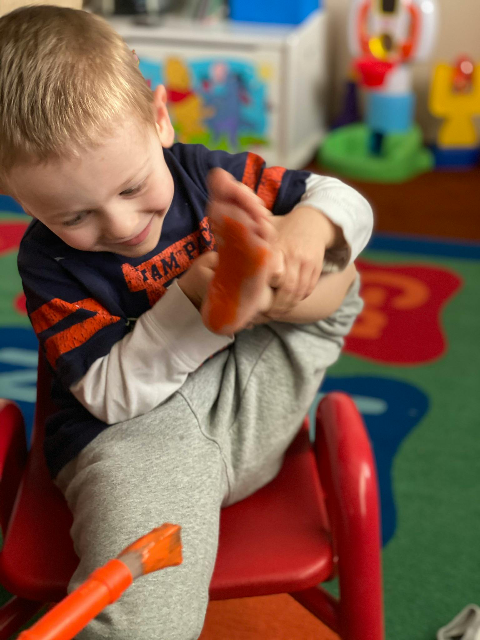 Child sitting on a red chair, holding their foot