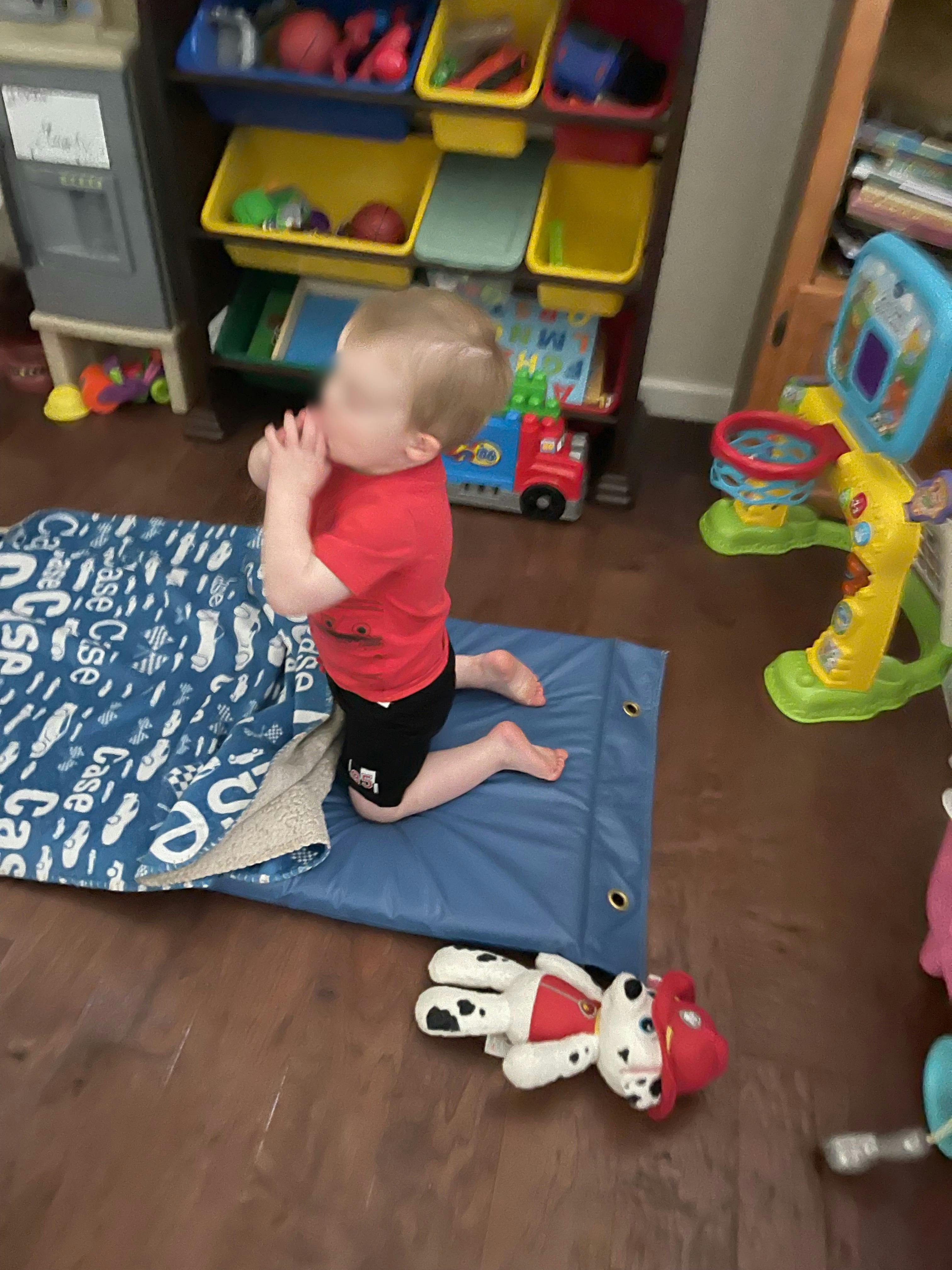 Child kneeling on a blue mat with hands near face