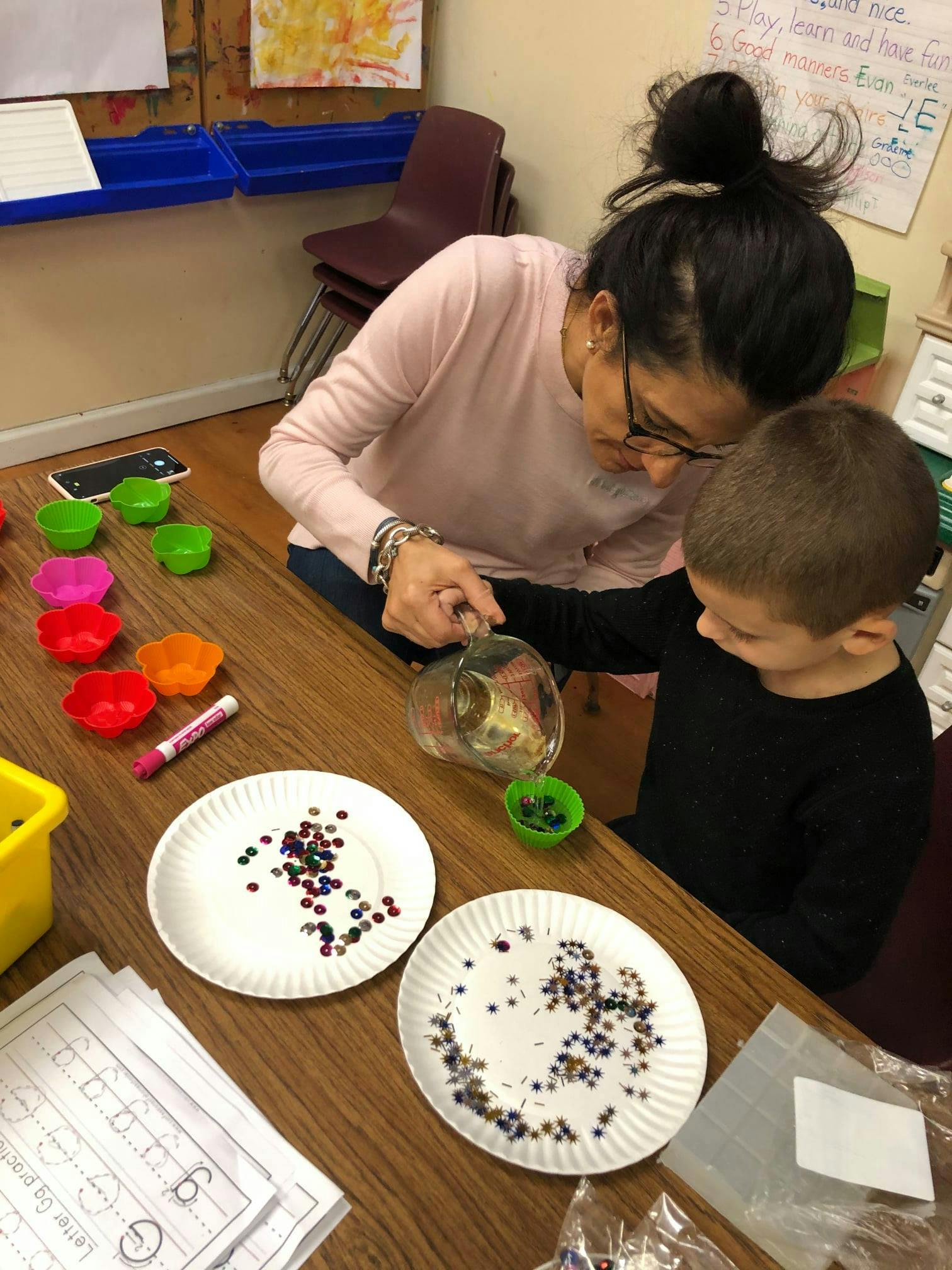 Person helping a child pour beads from a pitcher into a small cup