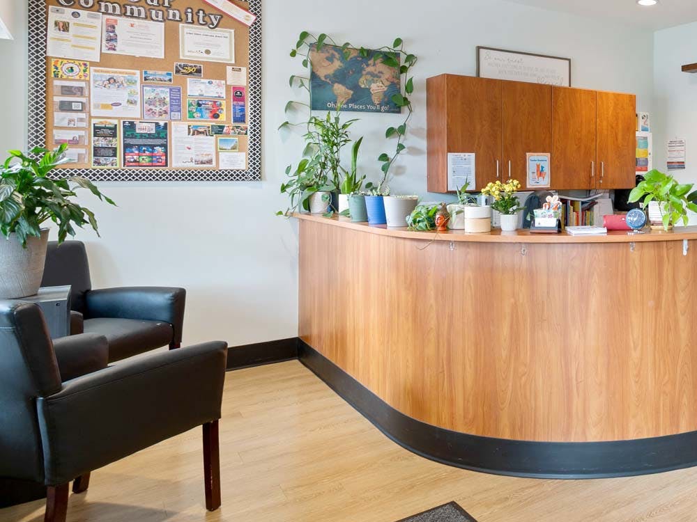 Reception desk with plants, two armchairs, and a community bulletin board