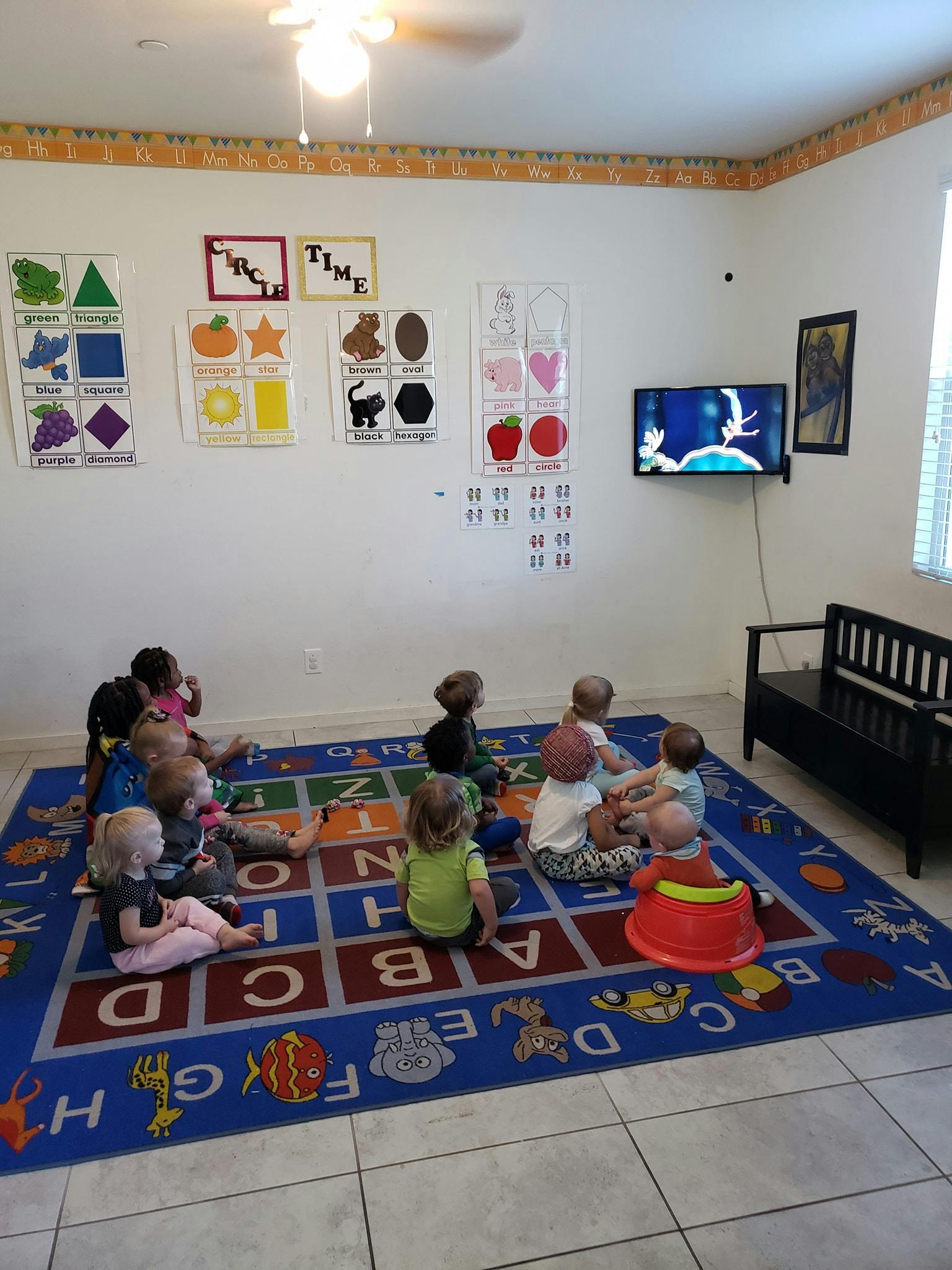 Children sitting on an alphabet rug watching television in a classroom