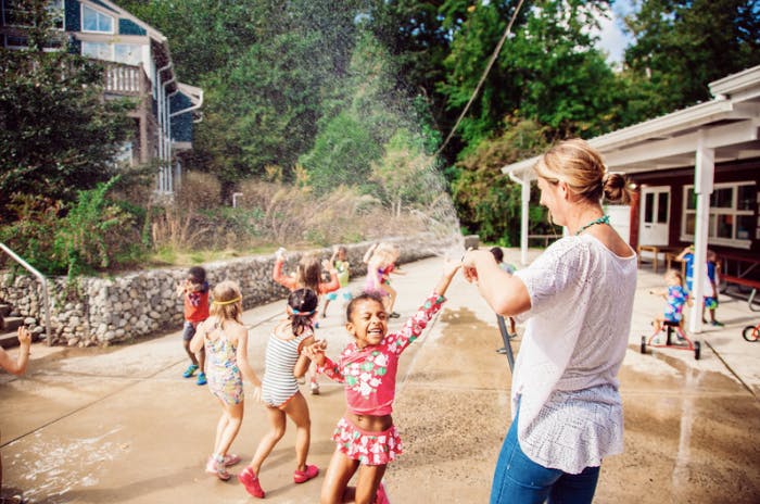 Person holding a hose spraying water on children playing children