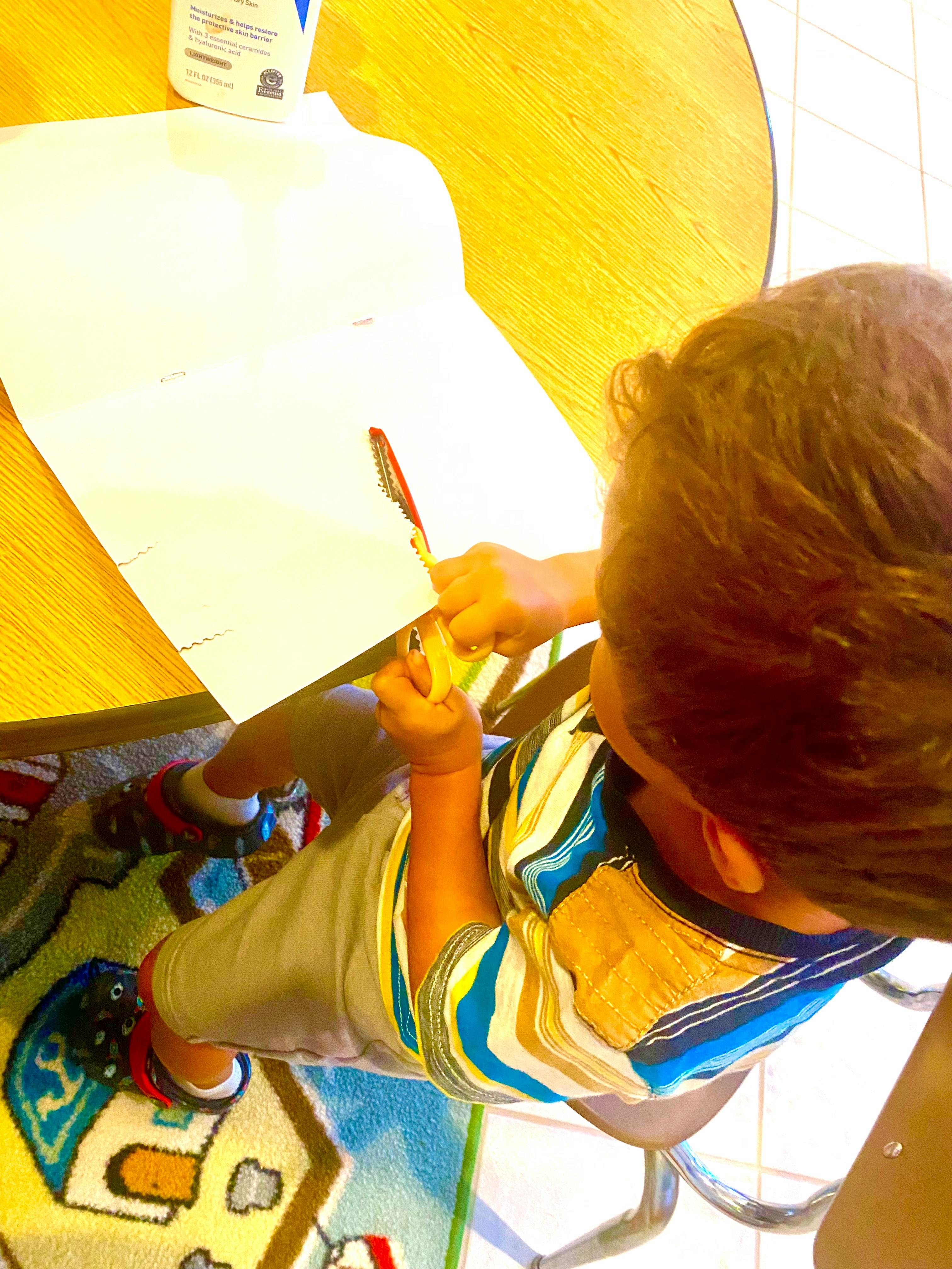 Child cutting paper with scissors at a table