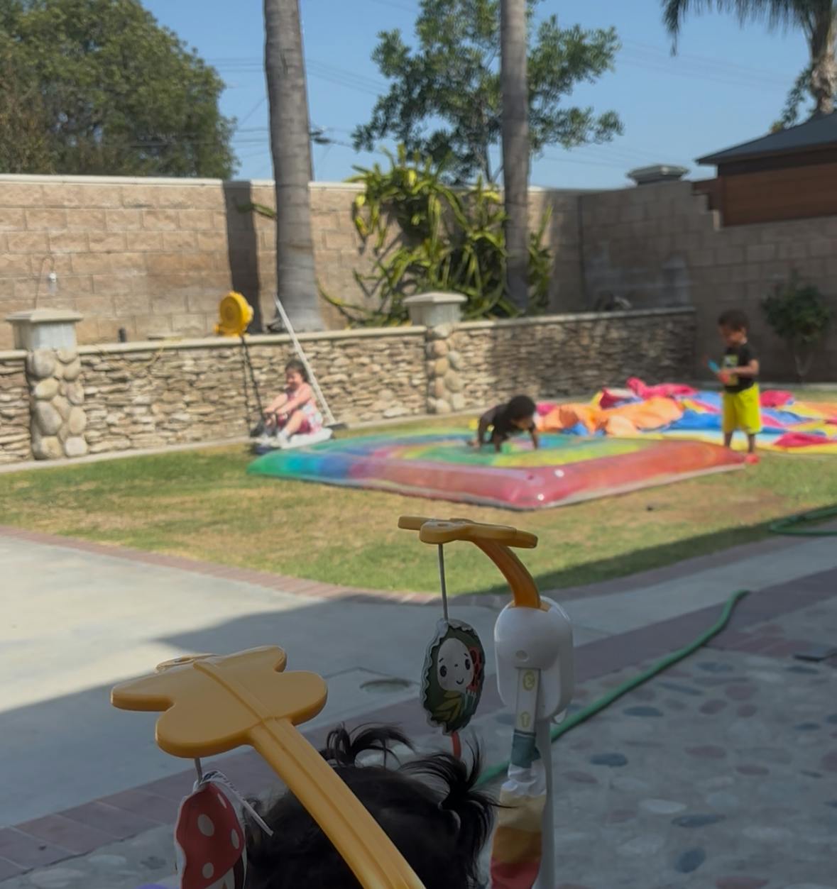 Children playing on a rainbow-colored inflatable water mat in a backyard
