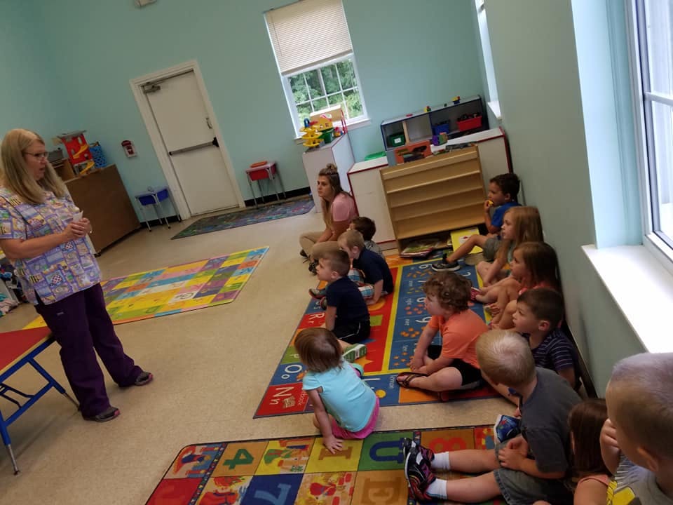 Adult speaking to a group of children sitting on rugs in a classroom