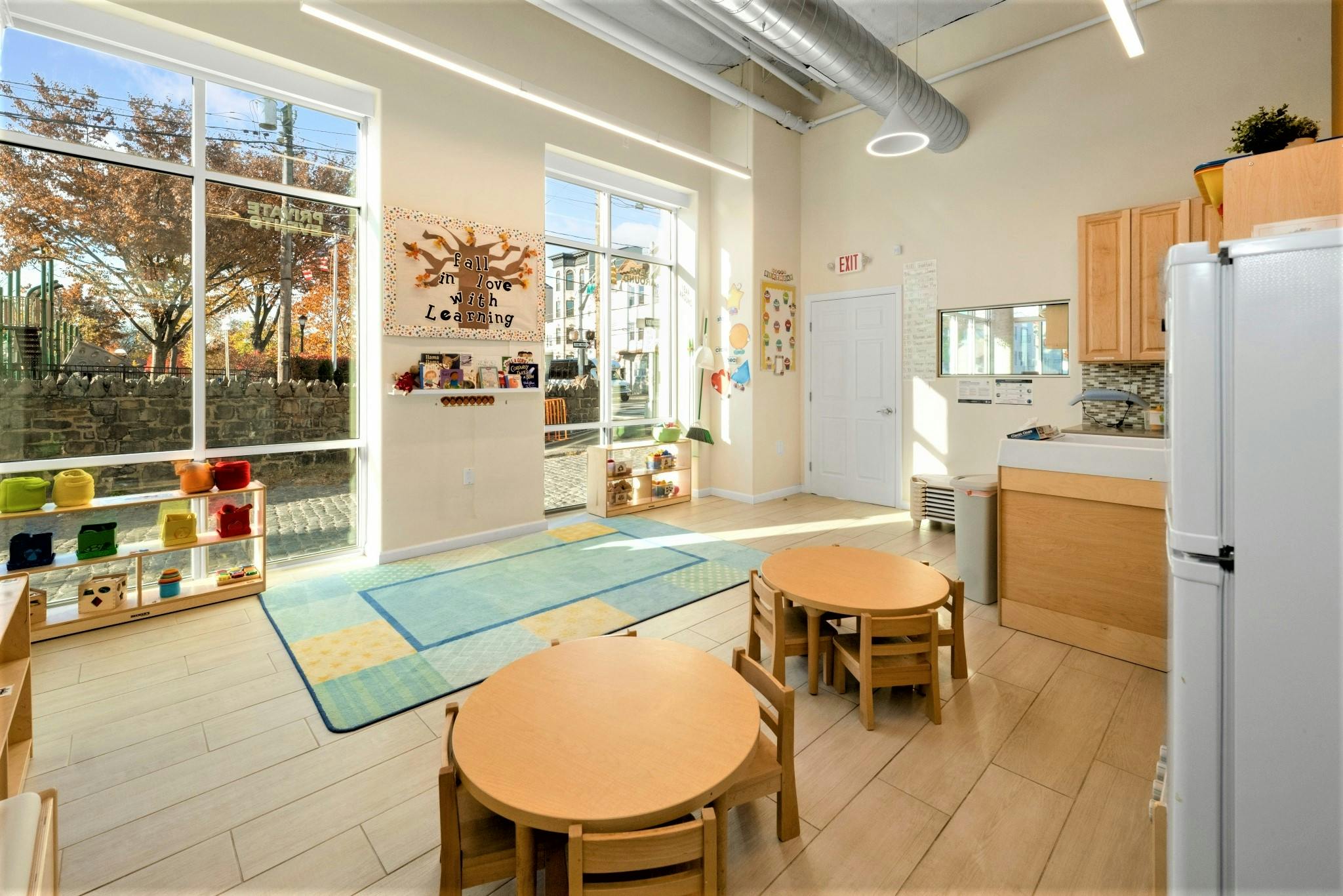 Classroom with small tables and chairs, large windows, and a play kitchen area