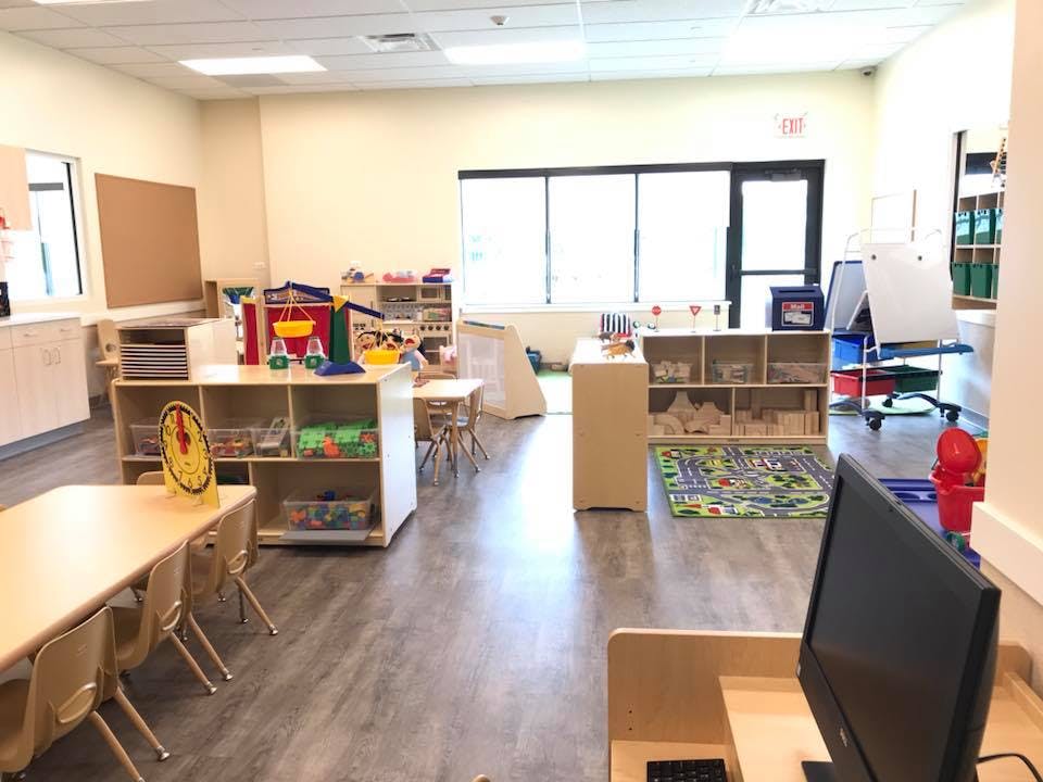 Classroom with small tables and chairs, shelves with toys, and large windows