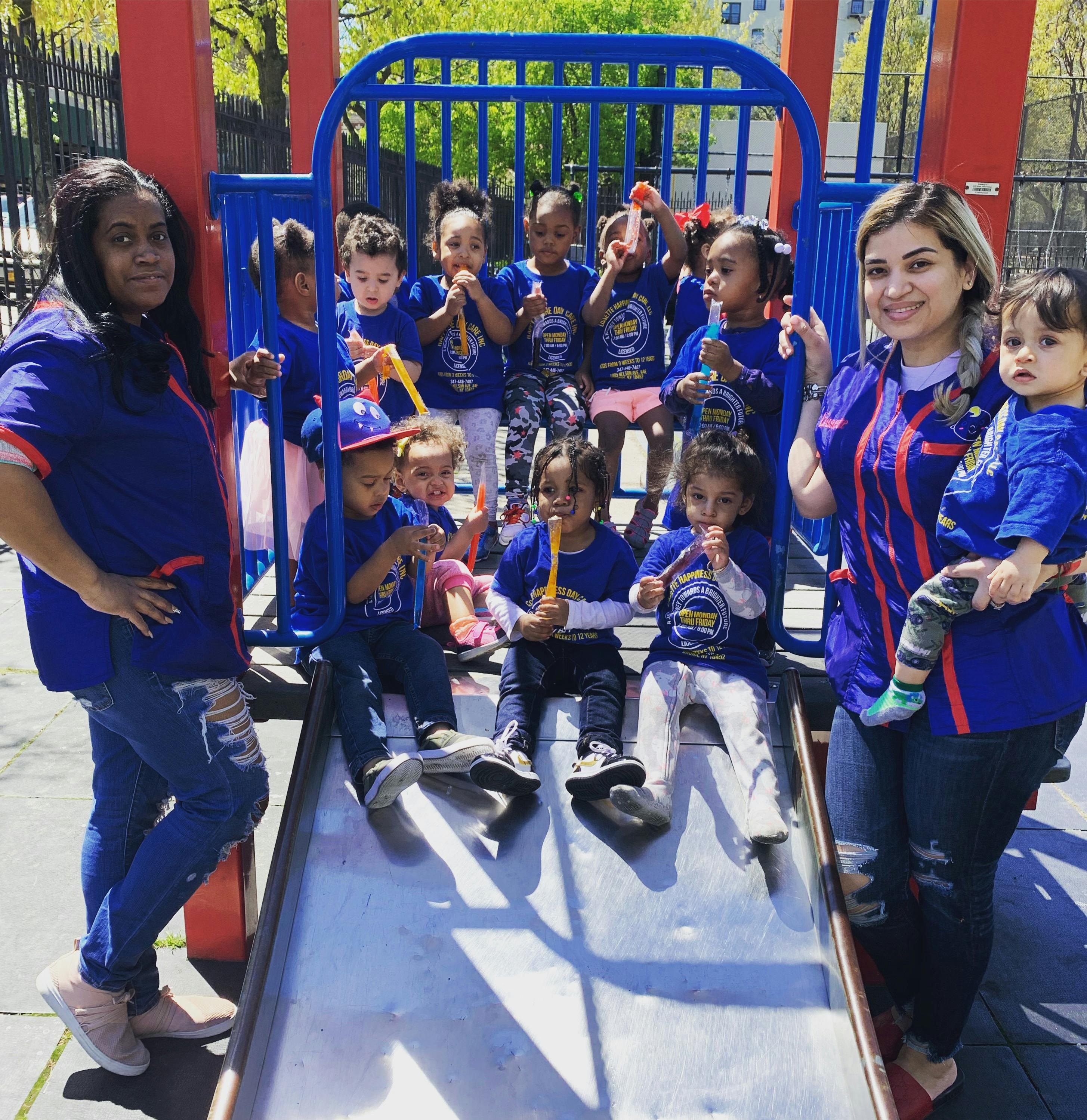 Two people with a group of children on a playground slide