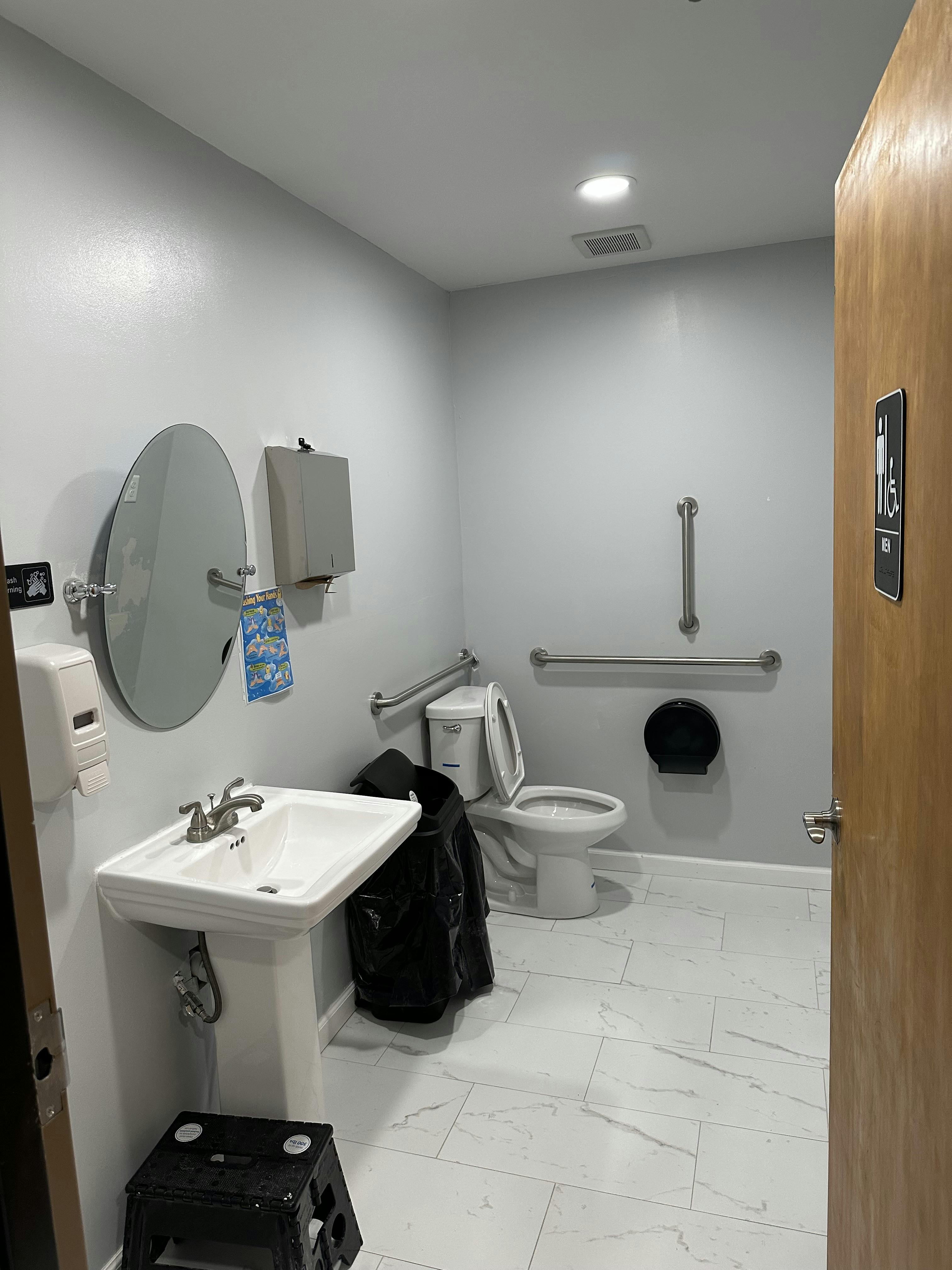 Public restroom with a toilet, sink, mirror, and grab bars