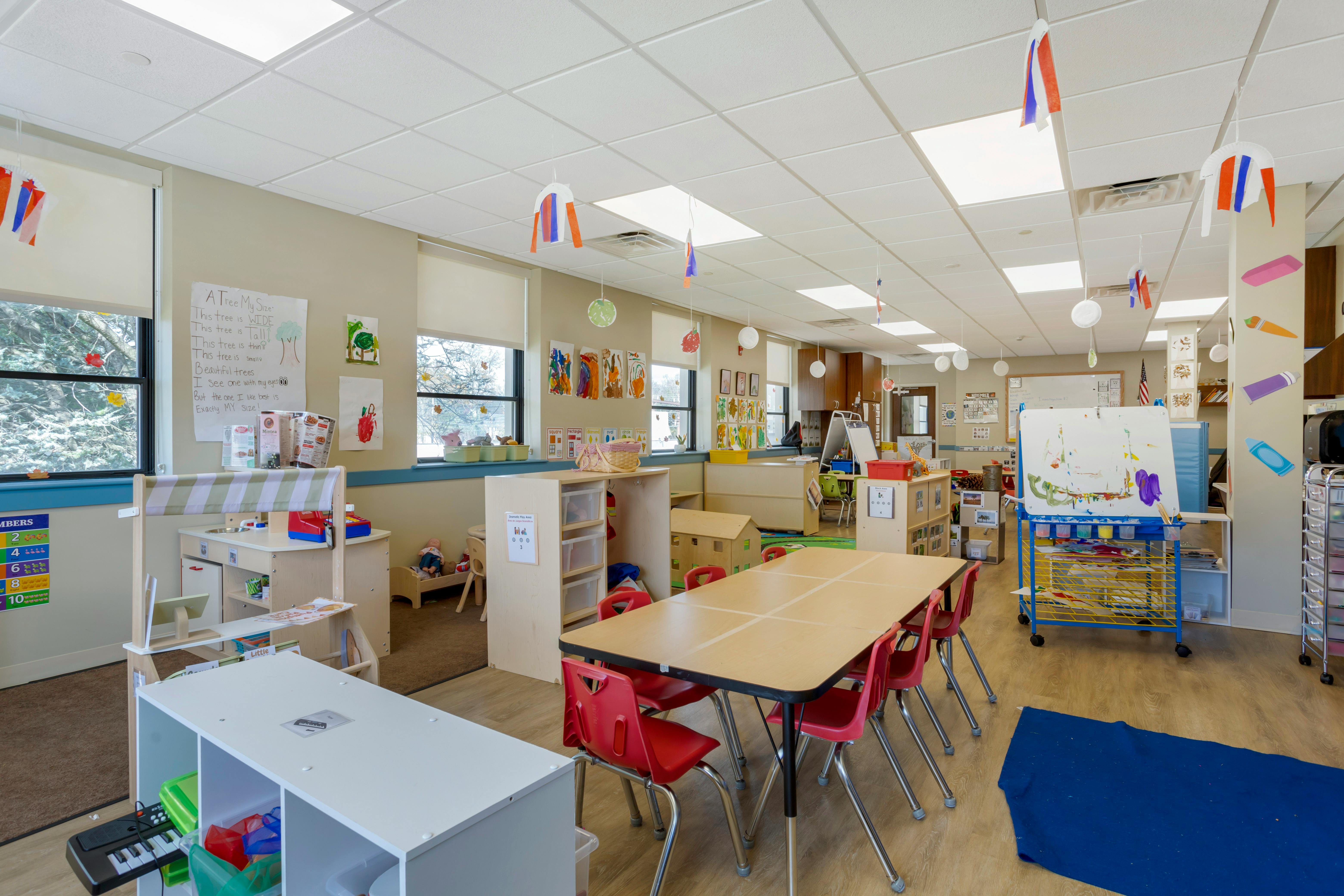 An empty early education classroom with tables, chairs, and play areas