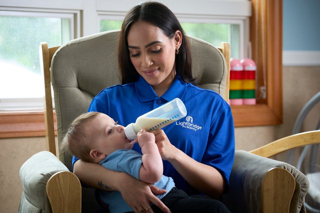 Person in blue shirt feeding a baby with a bottle