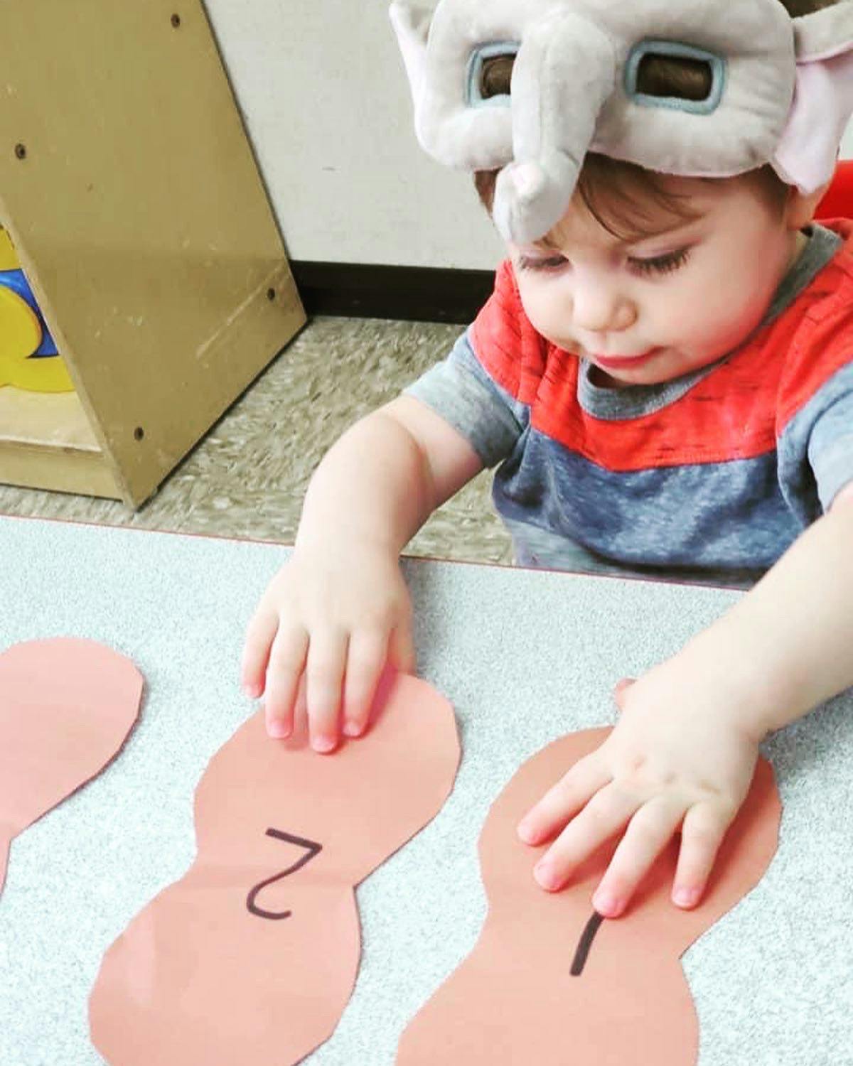 Child in elephant hat playing with paper cutouts