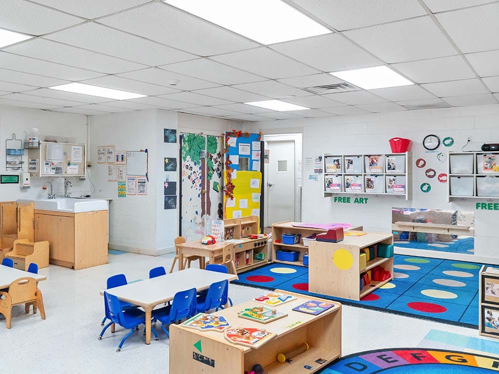 Empty colorful preschool classroom with small tables, chairs, and shelves