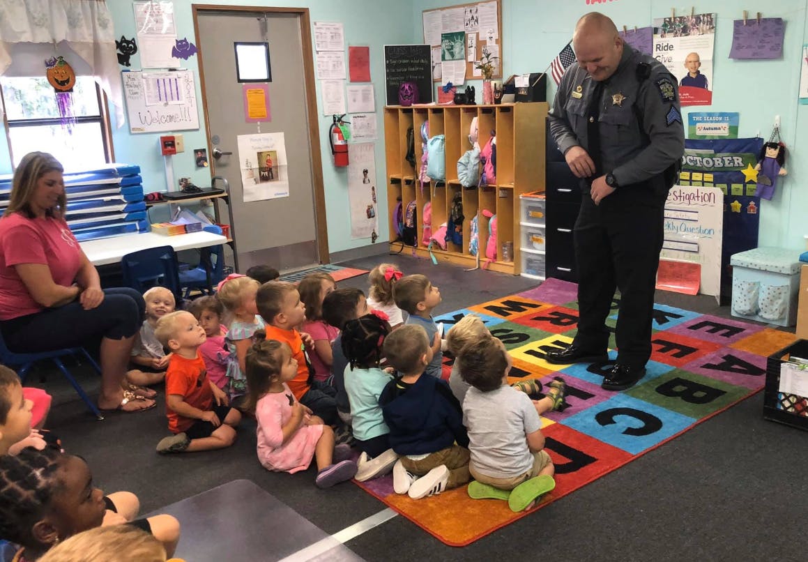 Police officer speaking to a group of children and an adult in a classroom