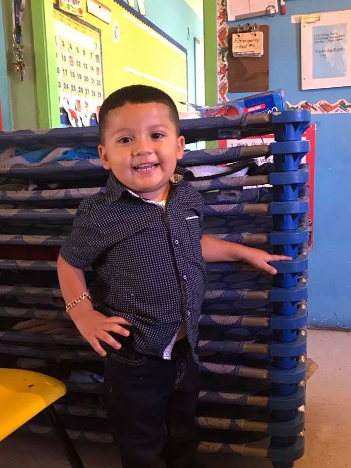 Child standing next to a stack of cots