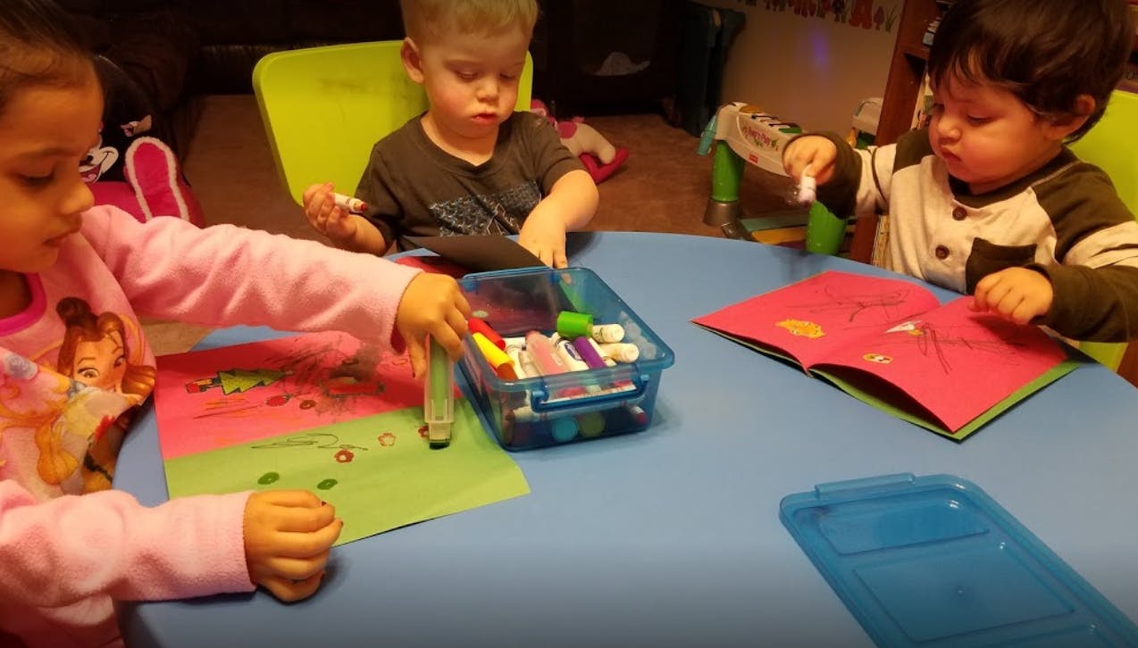 Three children drawing and looking at a book at a table