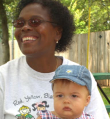 Person in sunglasses holding a child in a blue cap