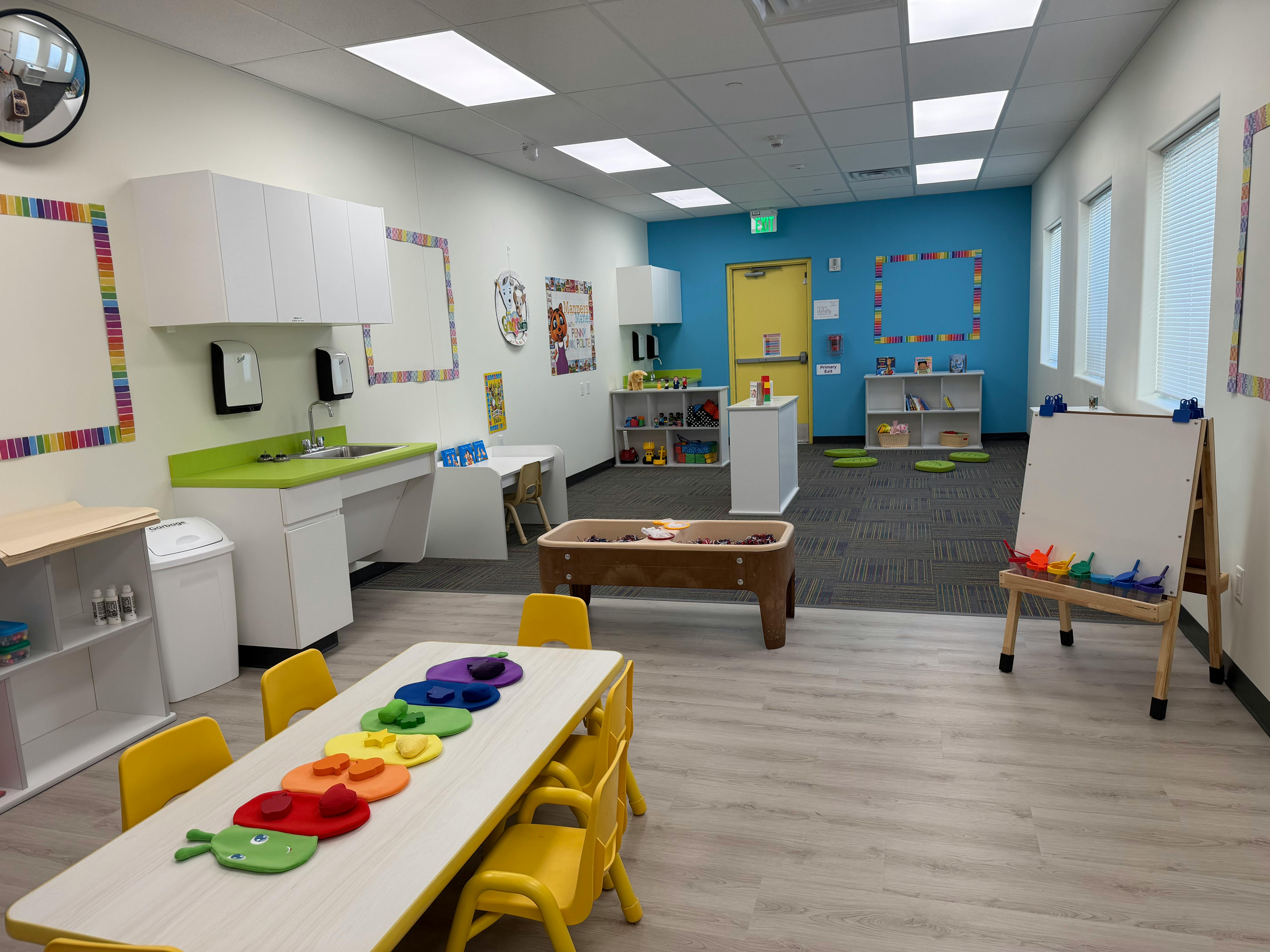 Bright classroom with small tables, chairs, and play areas