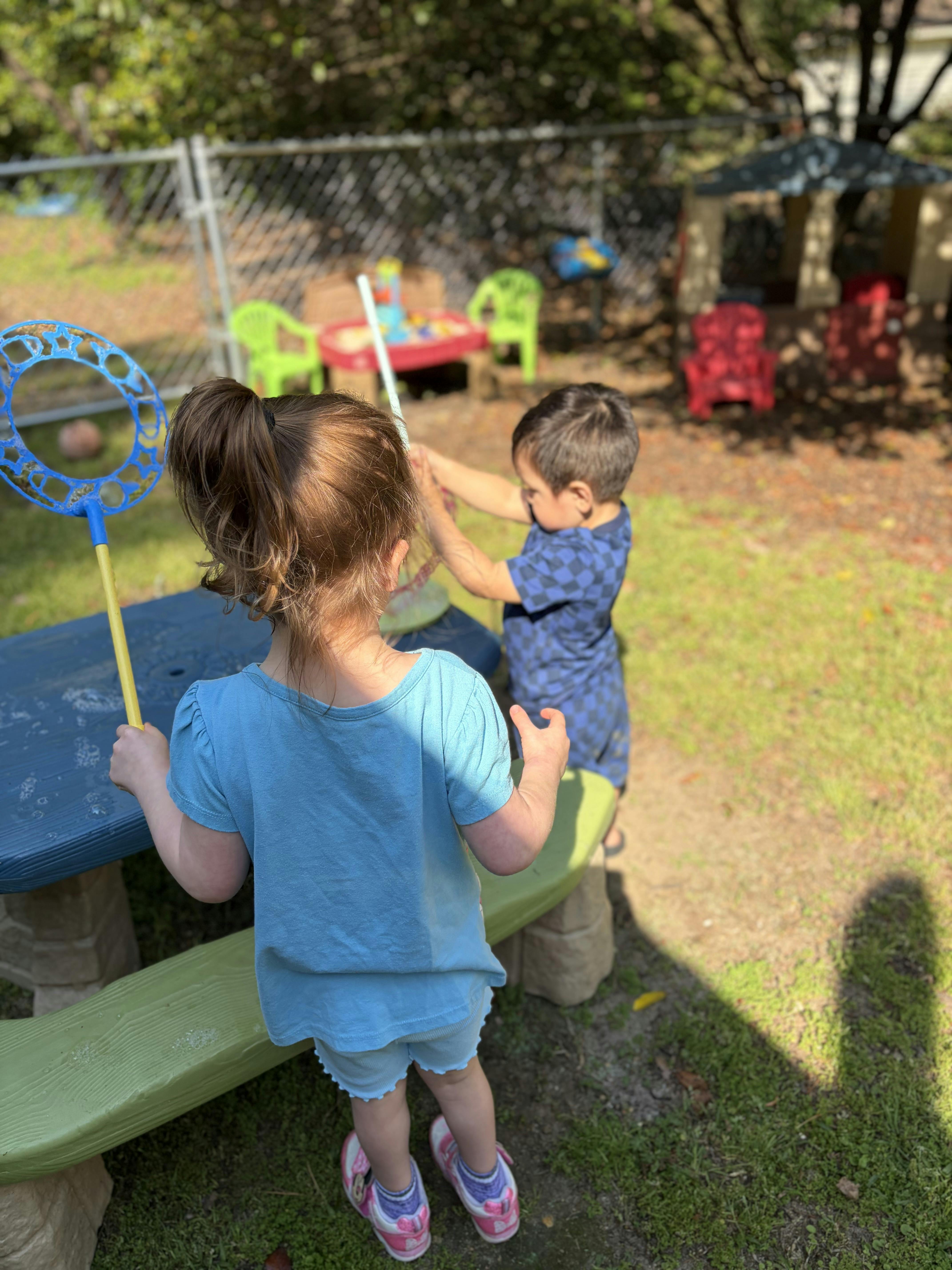 Two children playing with a bubble wand on a picnic table