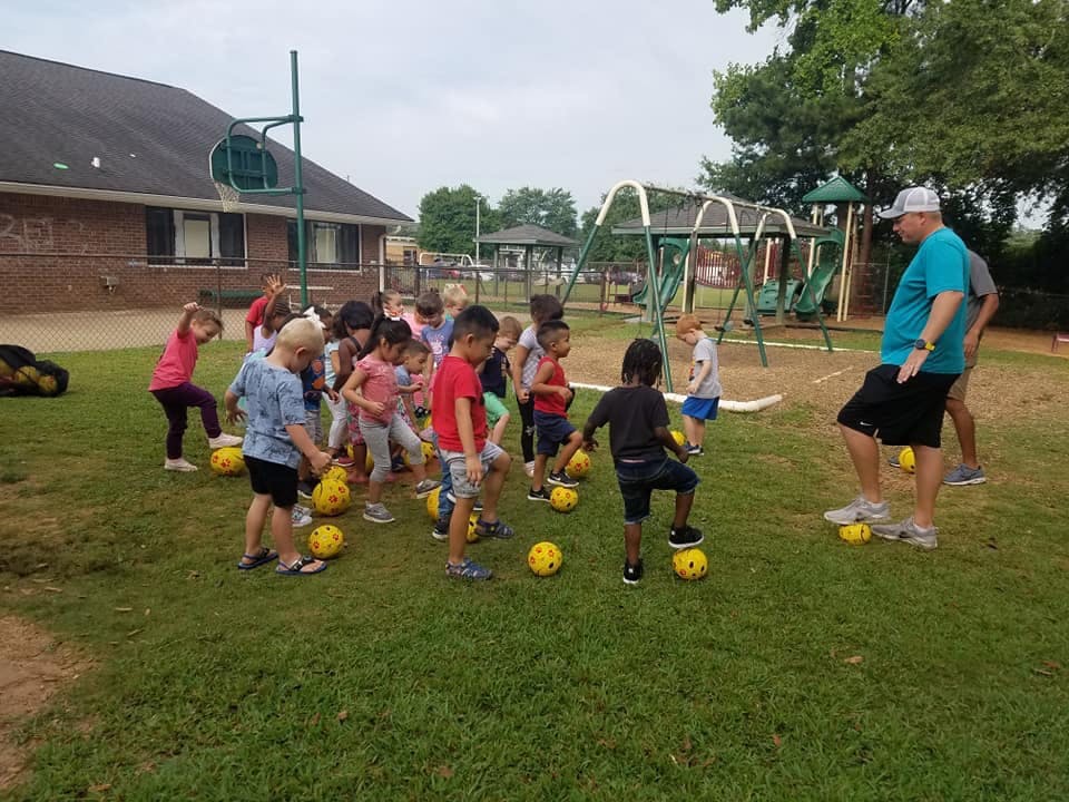 Adult and children playing soccer on a grassy field