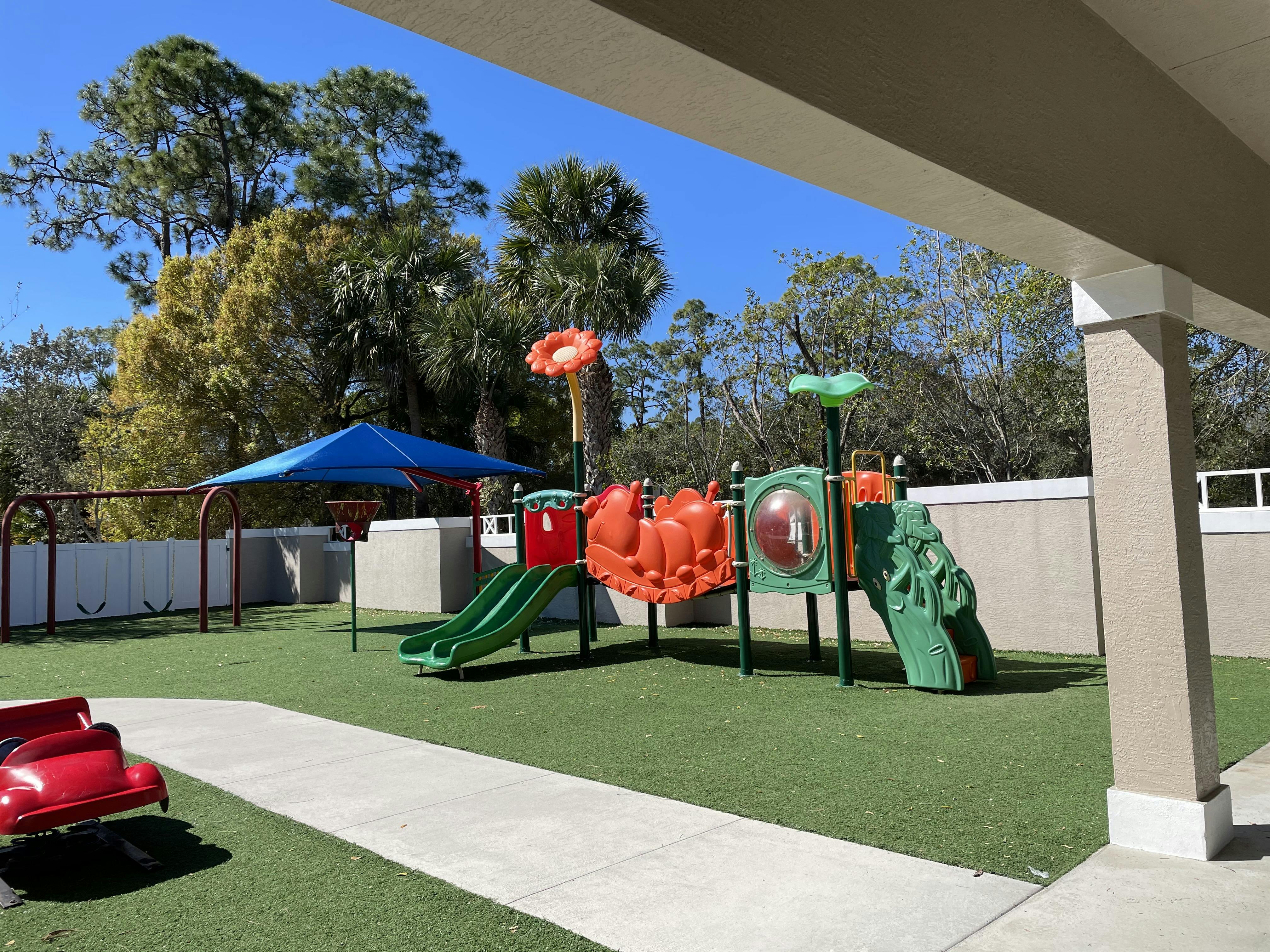 A playground with artificial grass, slides, swings, and a red spring rider