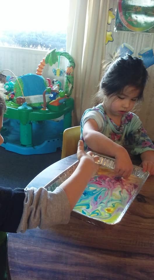 Child playing with colorful paint in a tray