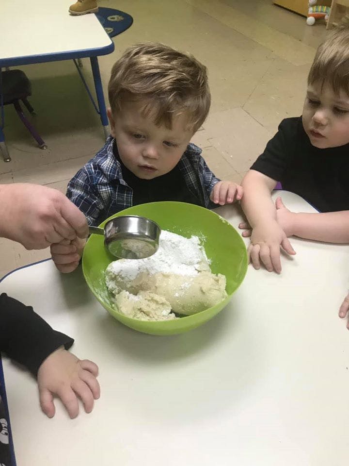 Two children watching a person add ingredients to a bowl