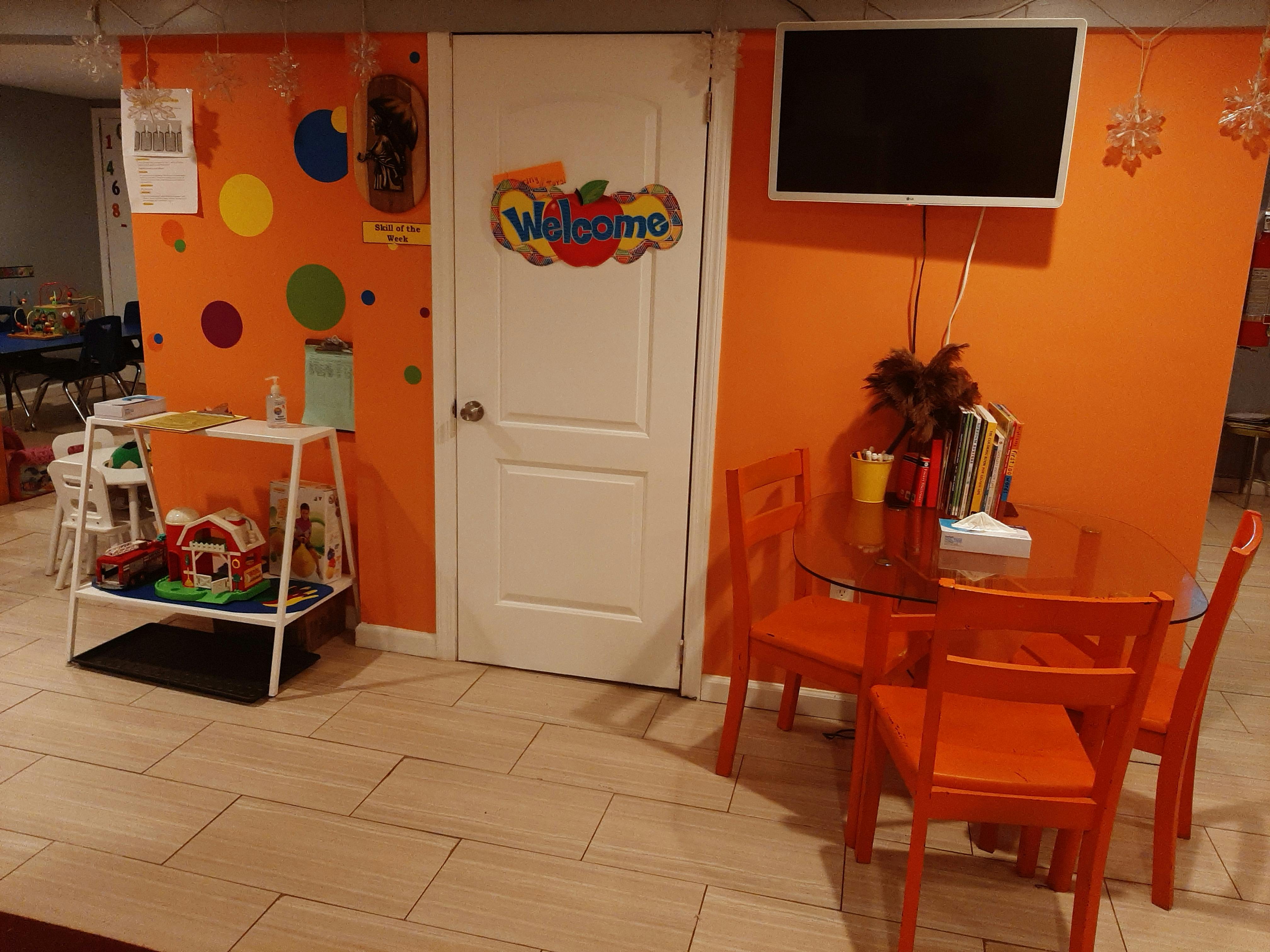 Room with orange walls, white door, small table with chairs, and toy shelf