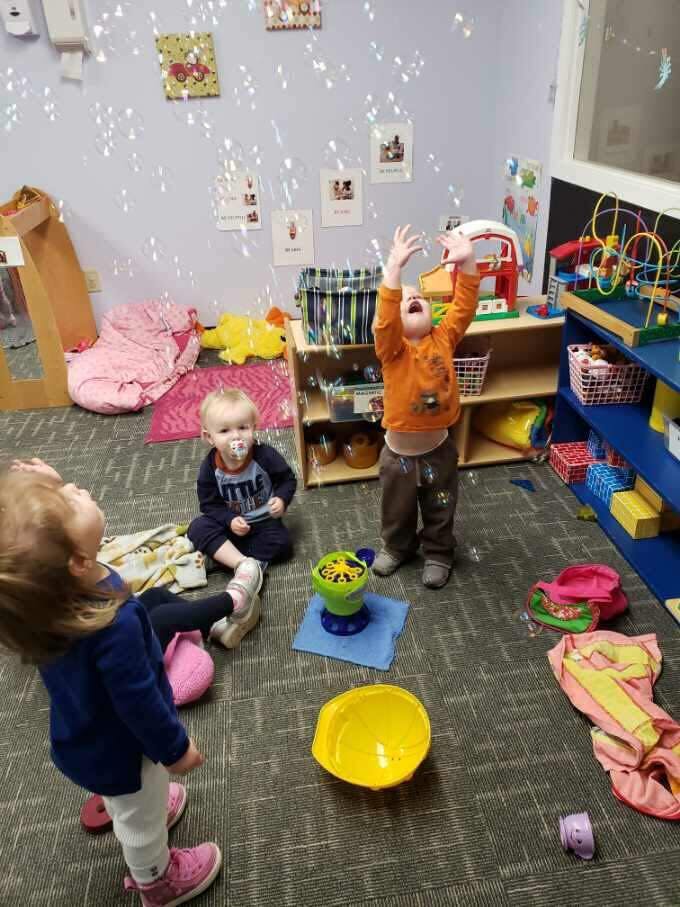 Three children playing with bubbles in a classroom