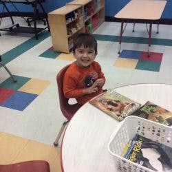 Child sitting at a table with books in a classroom