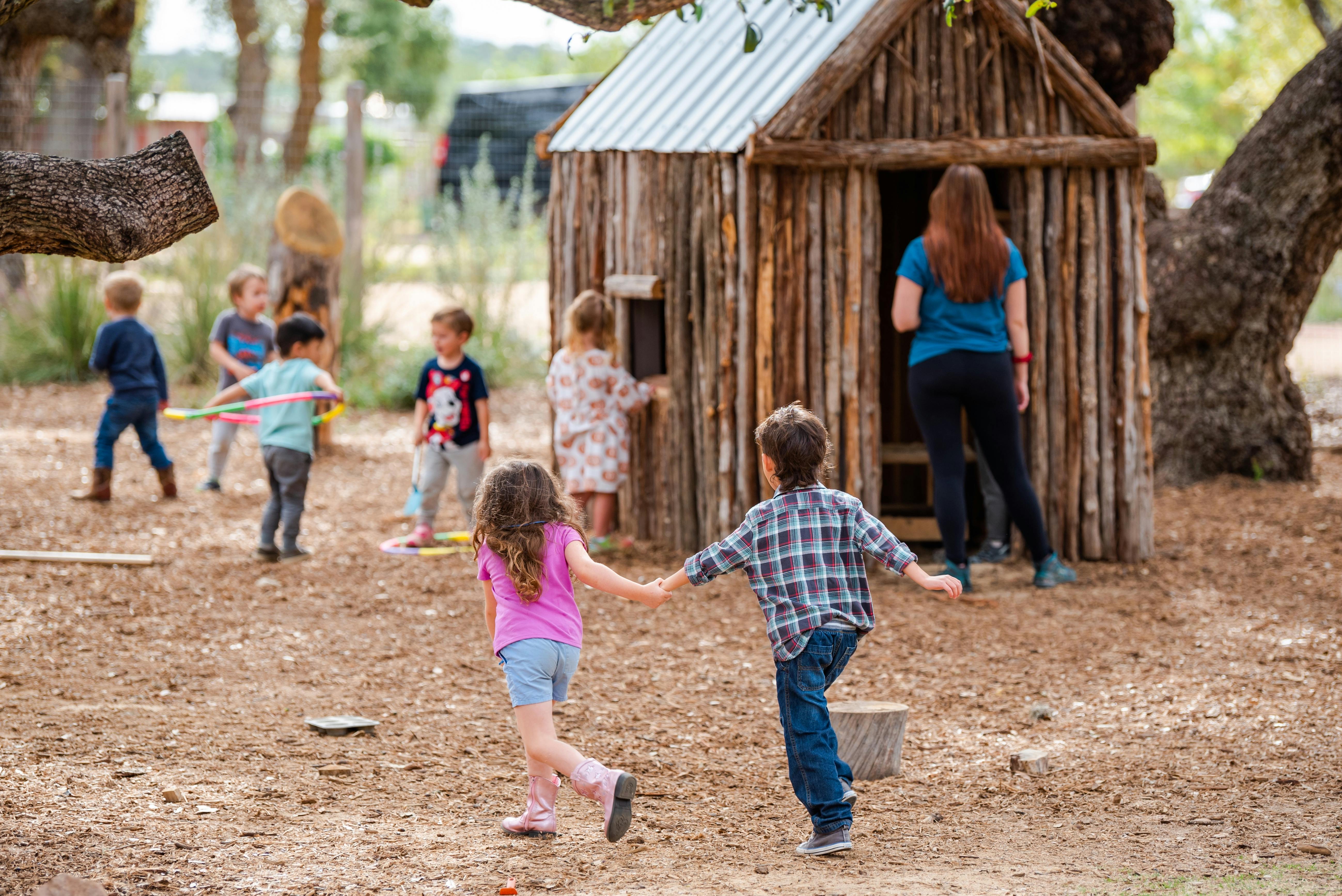 Children playing outdoors near a small wooden playhouse with an adult nearby