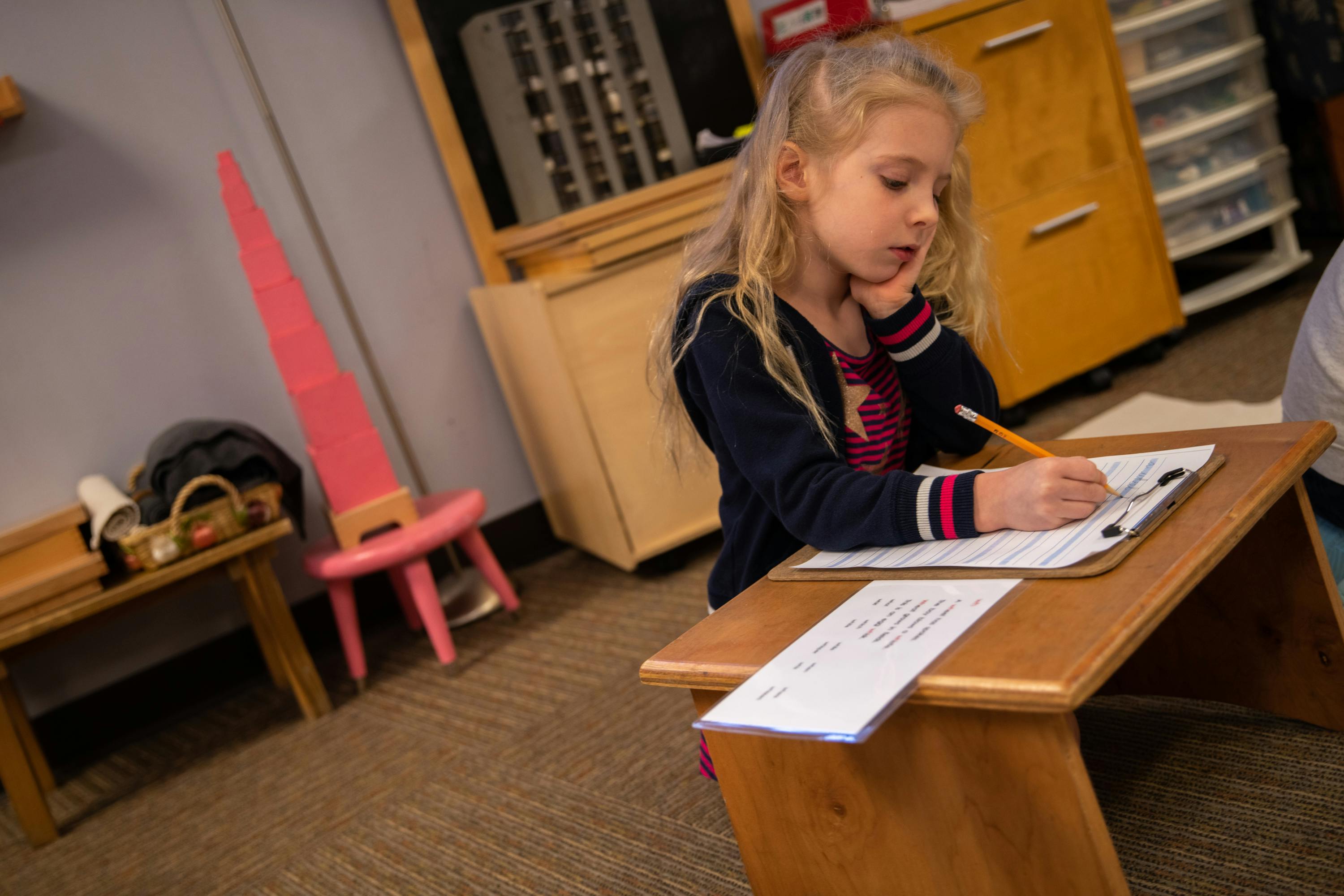 Child writing on paper at a small wooden desk