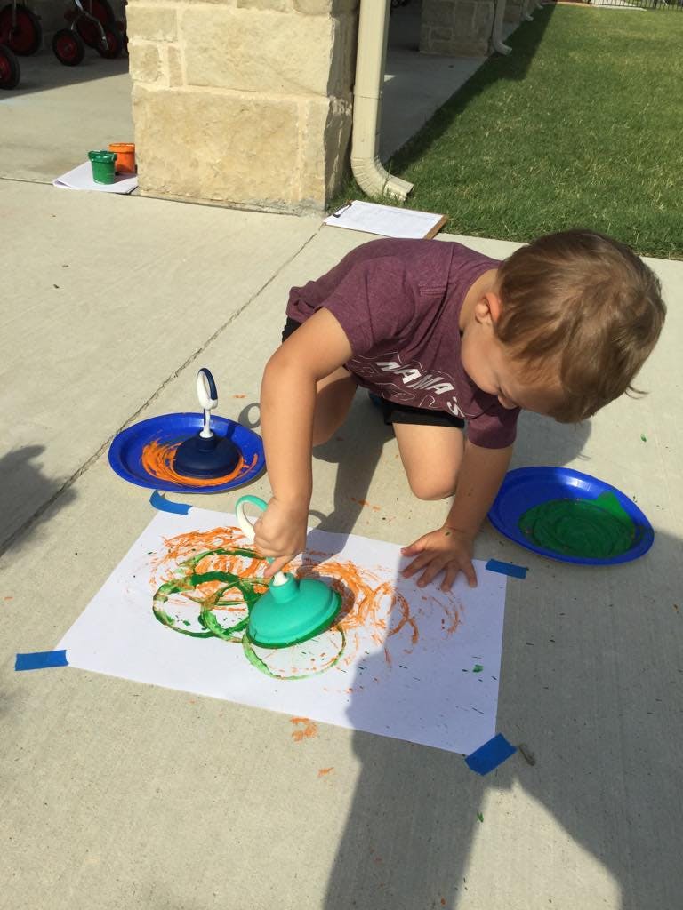 Child kneeling on pavement, drawing with a toy on paper