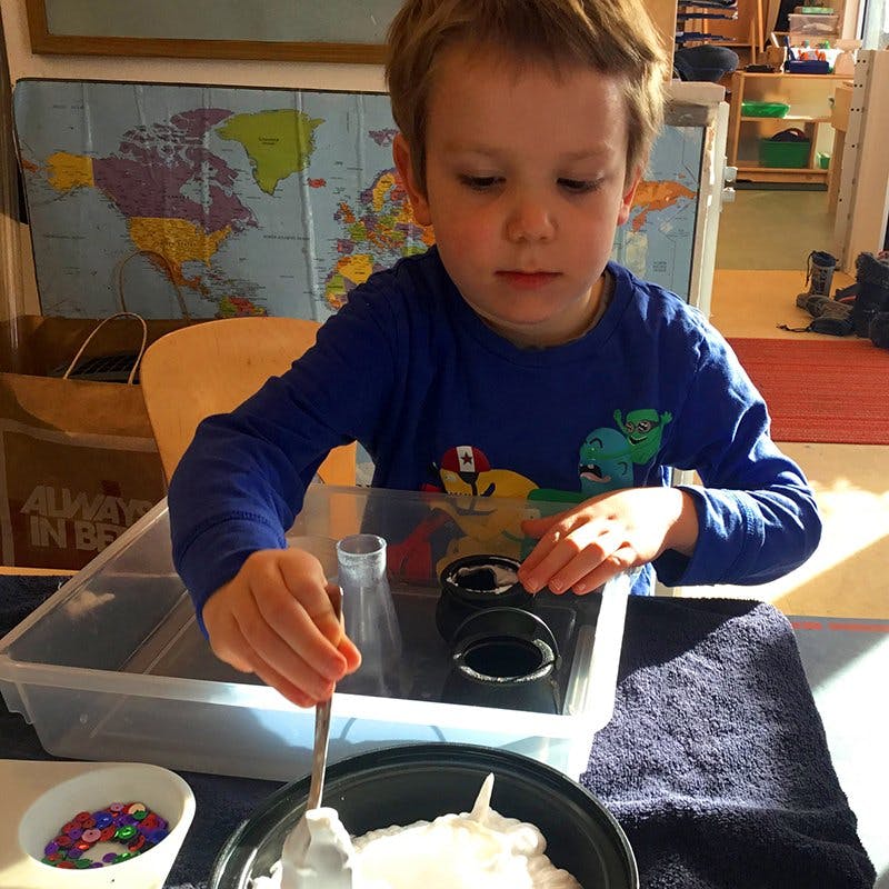 Child stirring white foam in a black bowl with a spoon