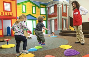 Two children playing on colorful stepping stones with an adult watching