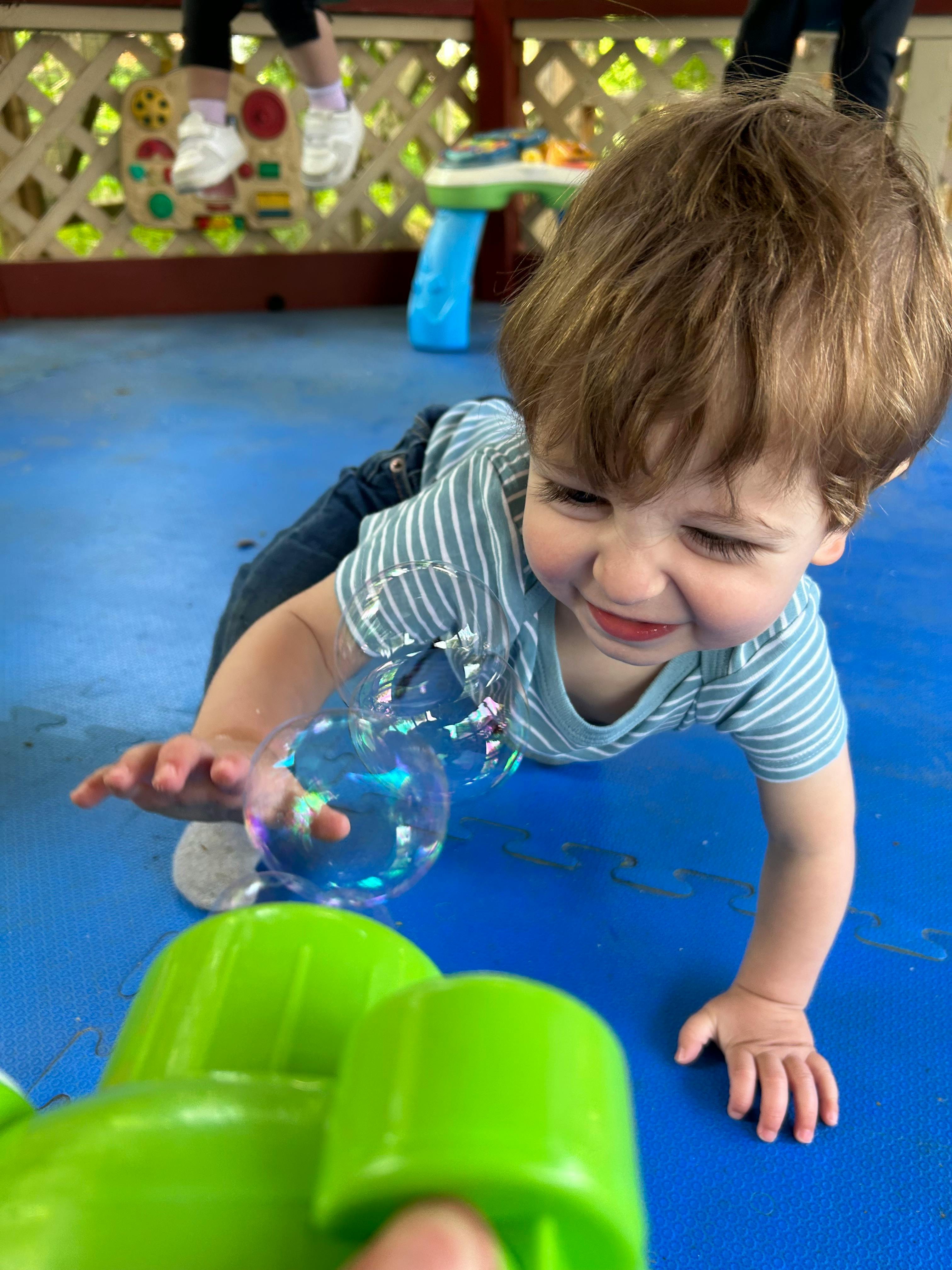 Child crawling on blue mat reaching for bubbles