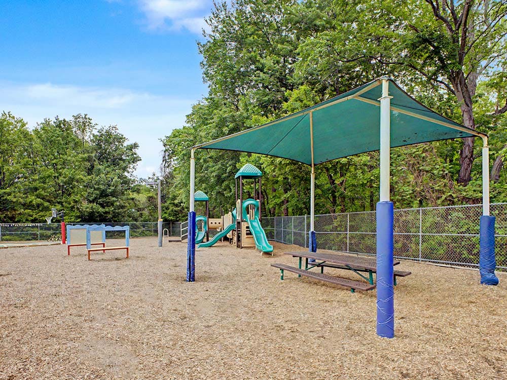 Outdoor playground with slides, swings, benches, and a shaded picnic table area