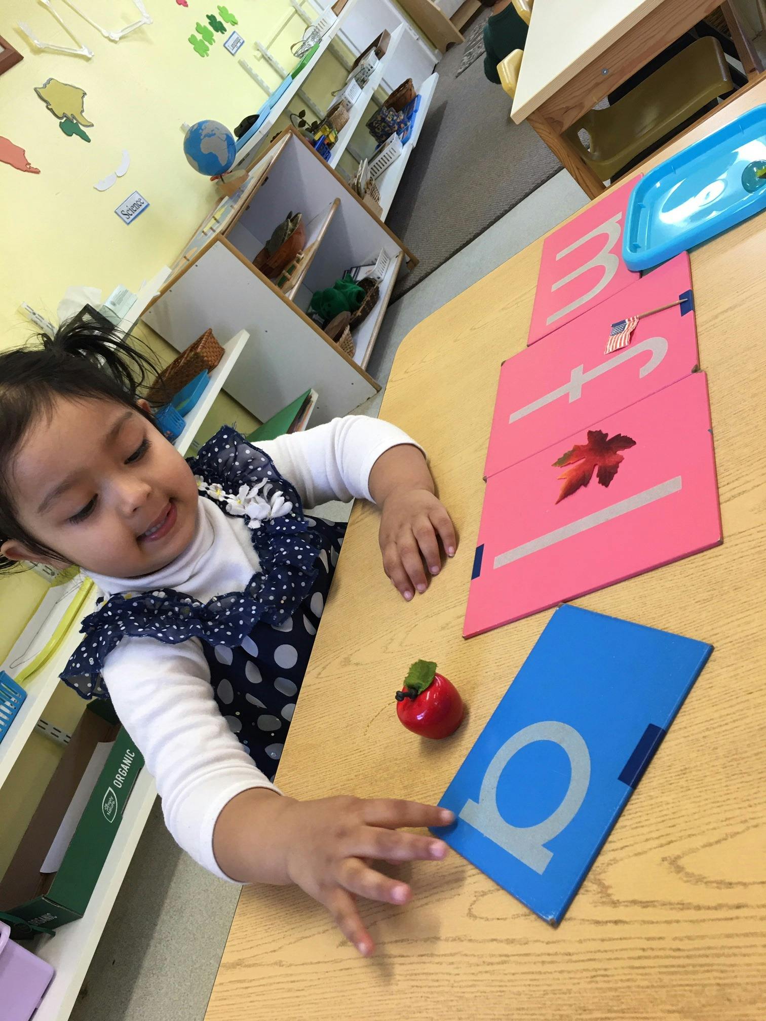 Child at a table with letter cards and a small apple