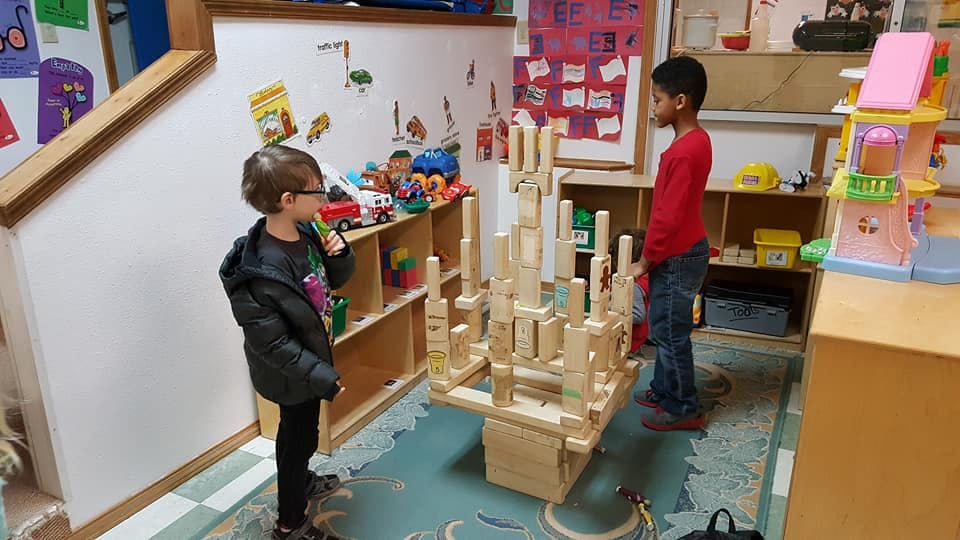 Two children standing near a wooden block structure in a classroom