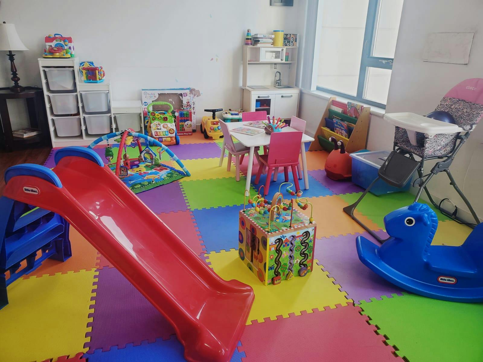 Indoor play area with a red slide, colorful floor mats, and various toys