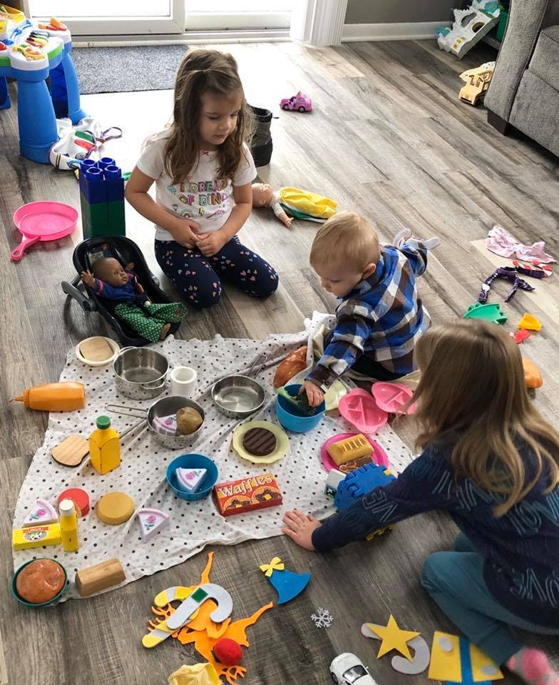 Three children playing with toy food and kitchenware on a blanket