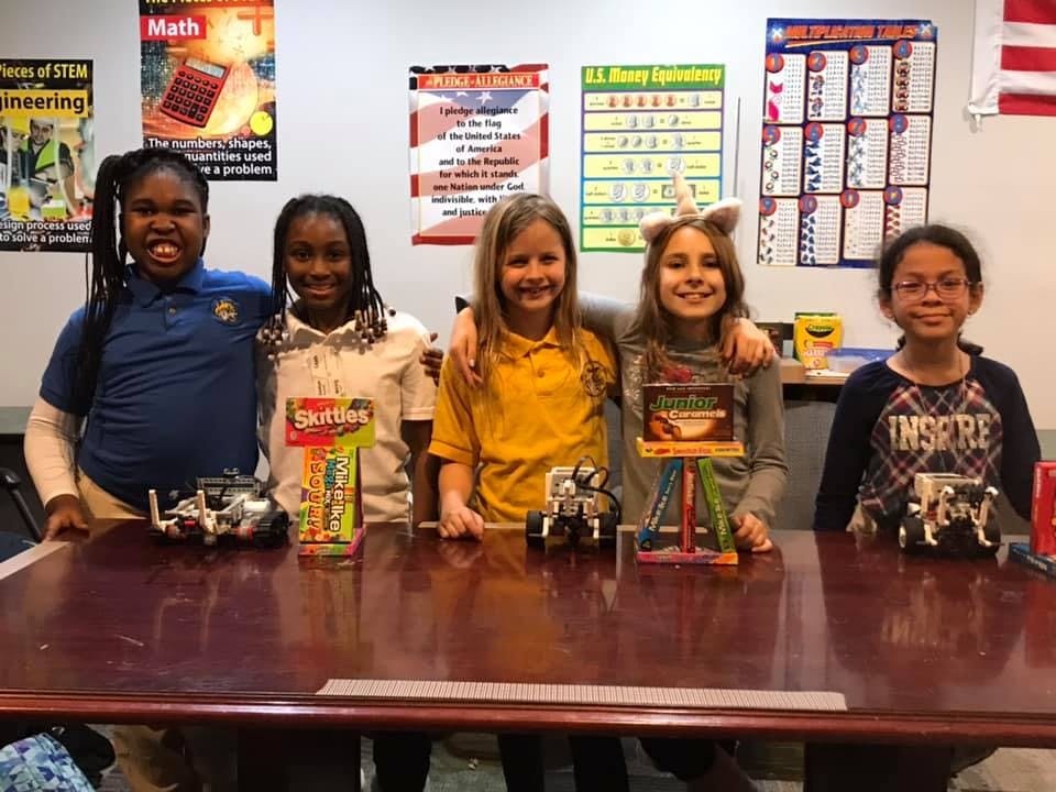 Five children standing behind a table with small robots and projects