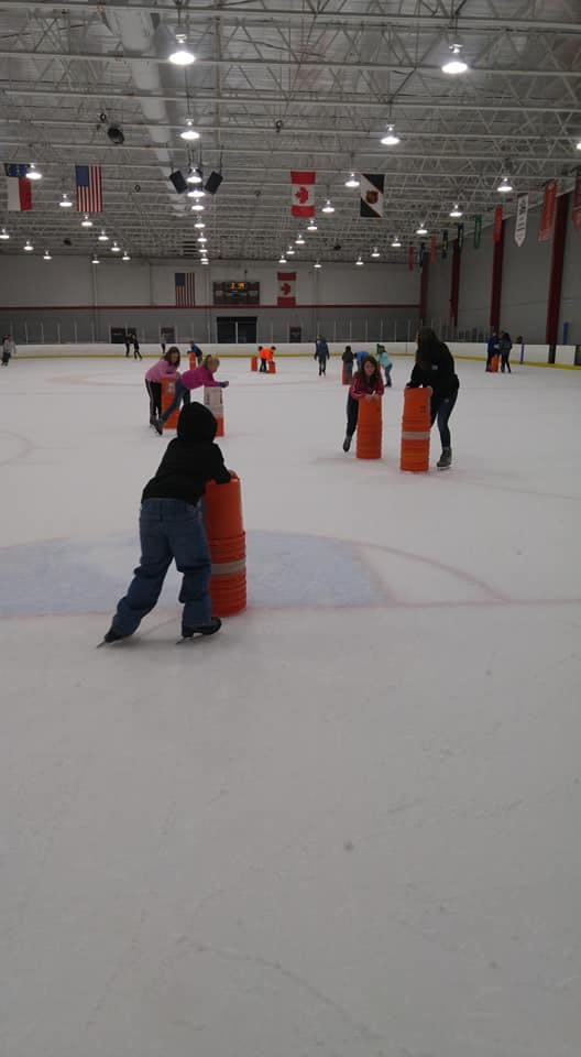 People ice skating with orange barrels on an indoor rink