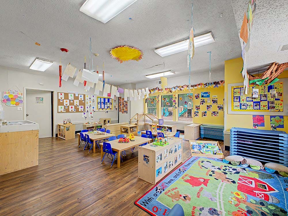 Classroom with small tables, chairs, and a play mat with barnyard animals