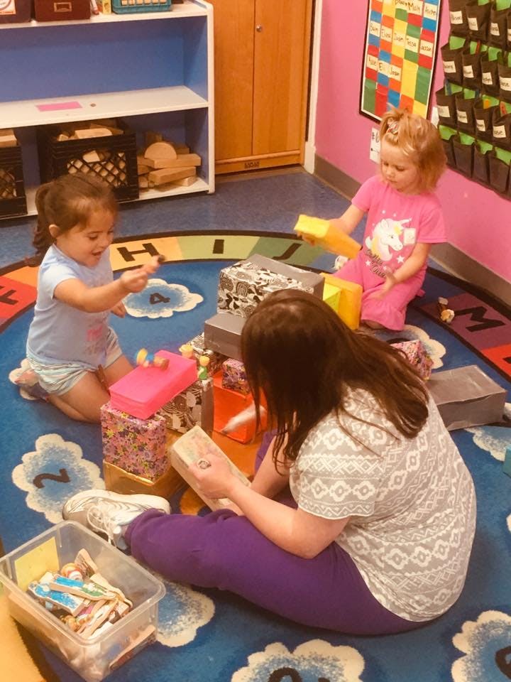 Two children and one person playing with blocks and reading on a rug