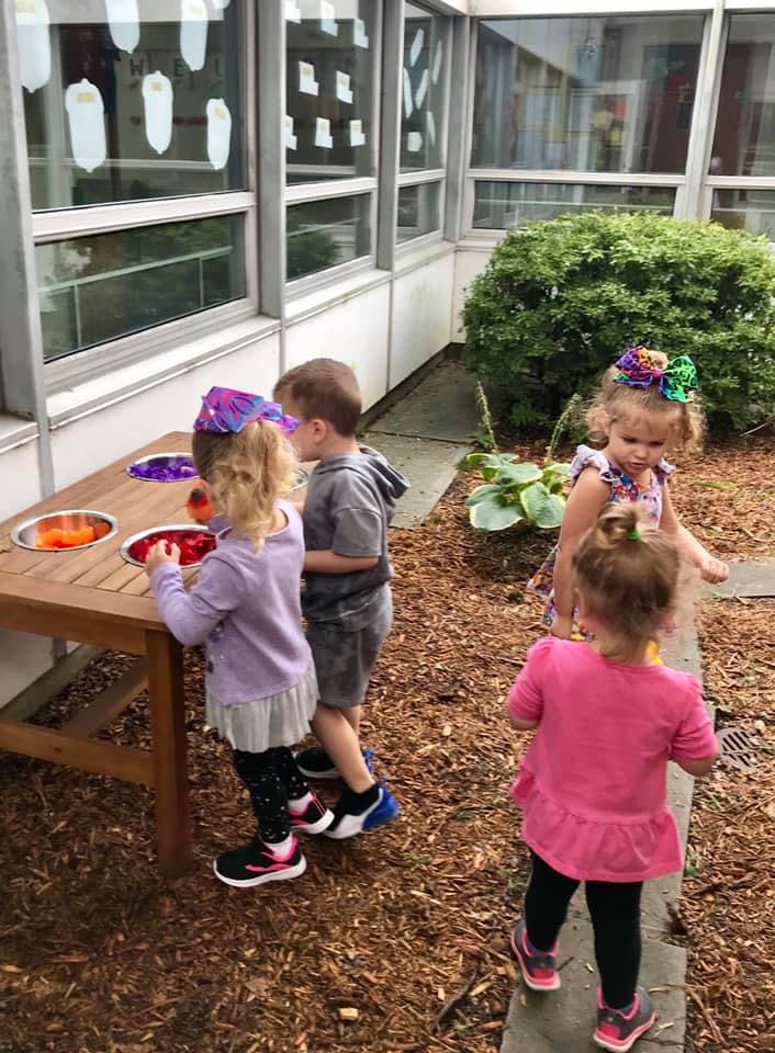 Children playing with items in bowls on a wooden table outdoors