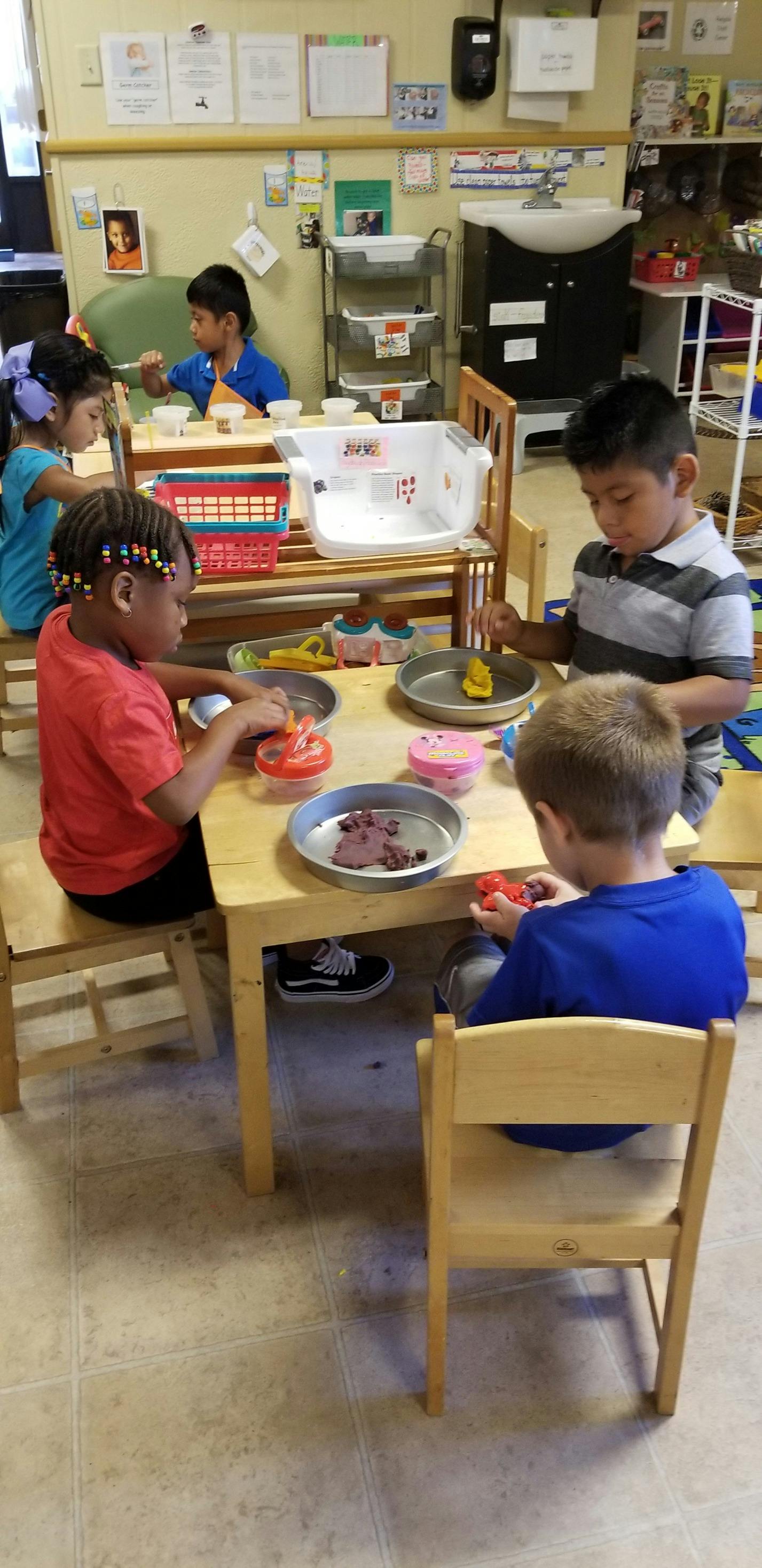Children playing with modeling clay at a table in a classroom