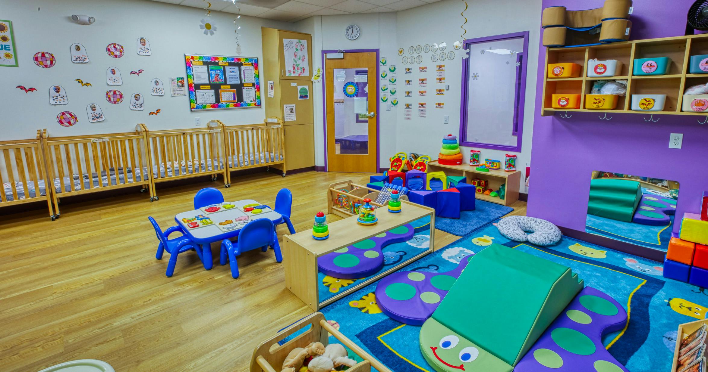 A classroom with cribs, a small table and chairs, and soft play areas