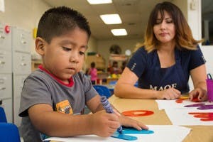 Child drawing at a table with an adult nearby